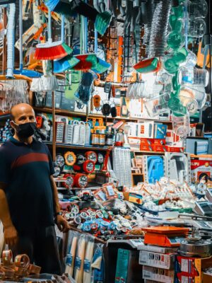 A man wearing a black facemask standing in a crowded hardware store filled with various tools and merchandise.