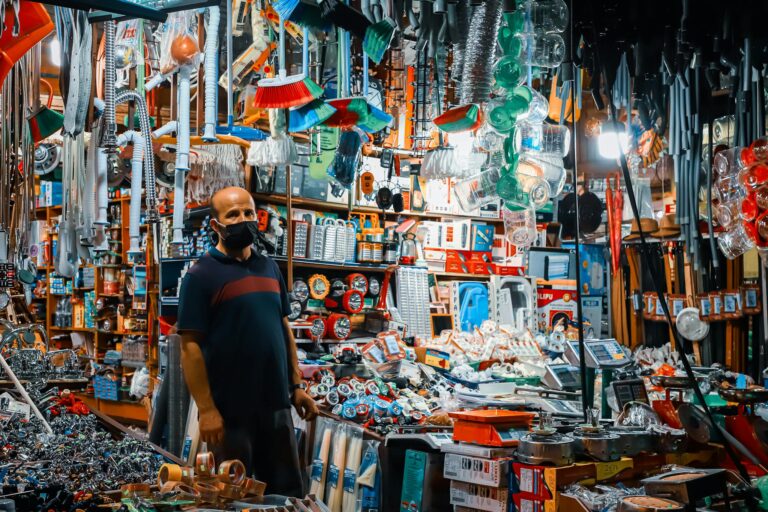 A man wearing a black facemask standing in a crowded hardware store filled with various tools and merchandise.
