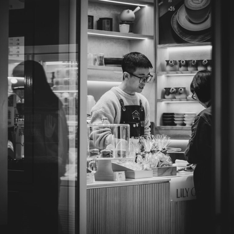 Black and white photo capturing a clerk assisting a customer inside a store, featuring various merchandise.